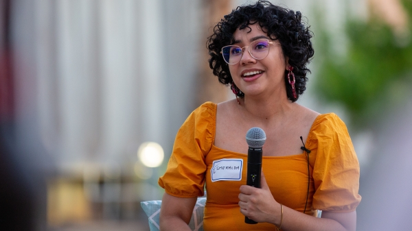 Woman with glasses and short, curly brown hair speaking into a microphone.