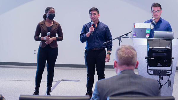 Three people standing on a stage speaking to a crowd.