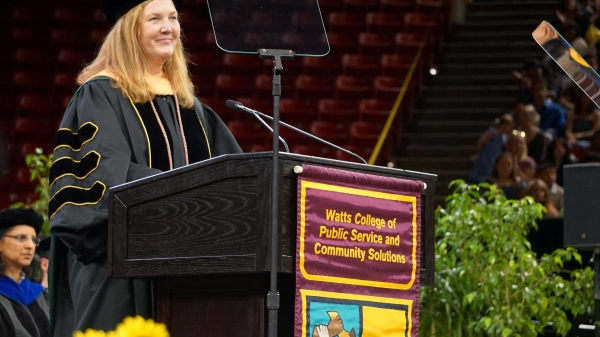 Beth Huebner in graduation robes standing behind a podium.