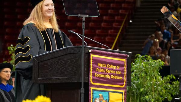 Beth Huebner in graduation robes standing behind a podium.