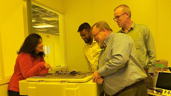A group of people looks at test circuitry on a table in a lab
