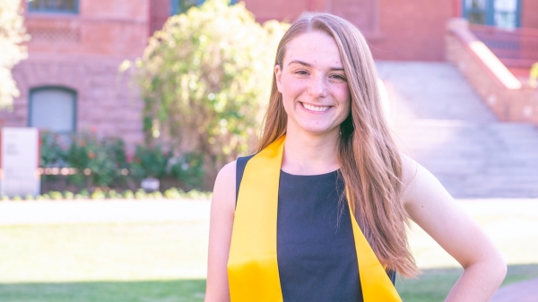 New ASU grad Miriam Goras poses in some of her graduation regalia in front of Old Main