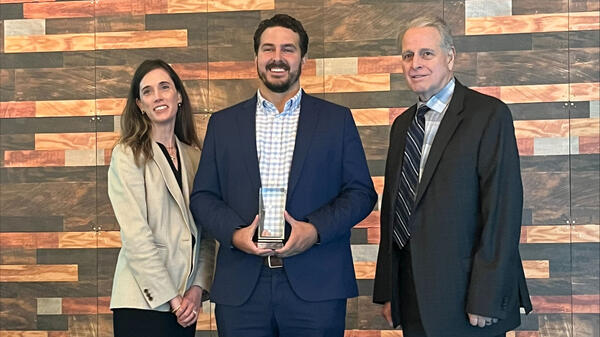 Group of three people posing for photo with middle person holding award