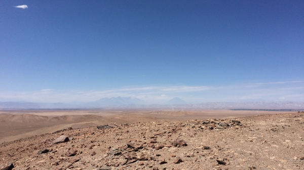 The rugged, flat, dirt of a desert terrain below with a bright blue sky above.