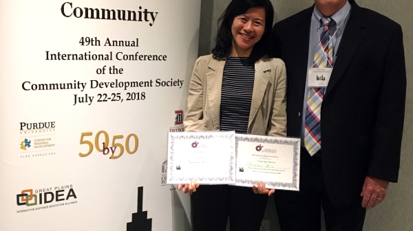 Chiamei Hsia stands with Richard Knopf in front of conference banner holding her awards