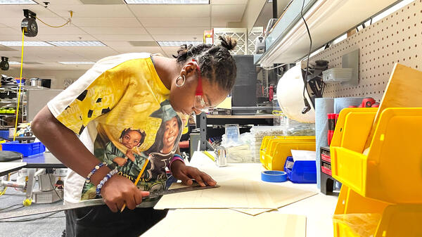 Person drawing on a piece of paper using tools in a lab.