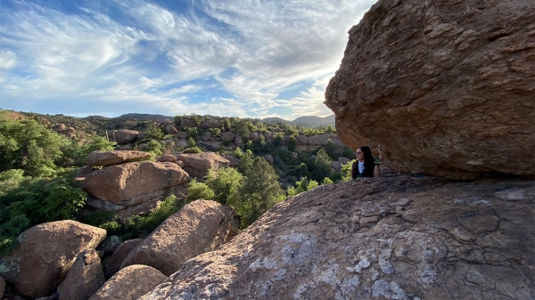 A woman looks out at a landscape while standing against several massive boulders