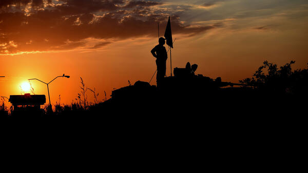 A man on top of military equipment is silhouetted against a sunset sky