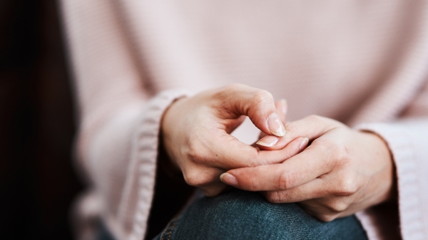 Close-up  view of a person's hands clasped on their lap.