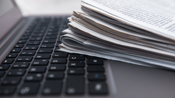 Newspapers stacked on top of open laptop