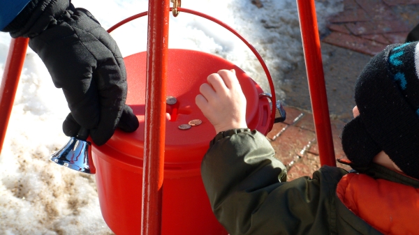 Young child puts change in a donation bucket.