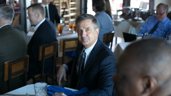 Stock photo of older man in dark suit sitting at table.