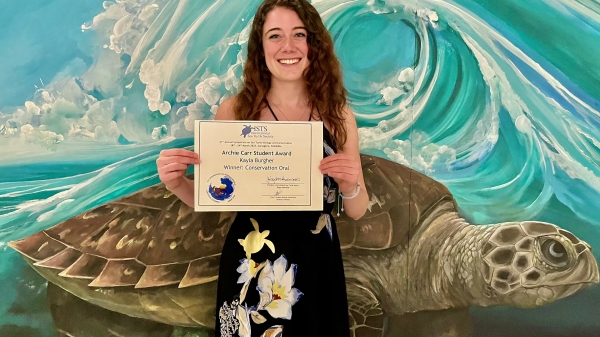 Kayla Burgher holds award in front of a sea turtle mural.
