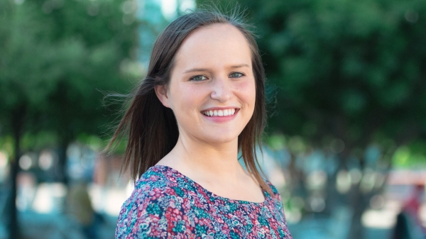 Kelly (with light complexion, brown hair, and pink and green floral blouse) smiles in Civic Space Park