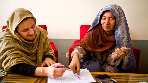 ASU Professor Rangina Hamidi seated at a table with another woman. Hamidi writes on a piece of paper while the other woman points at it.