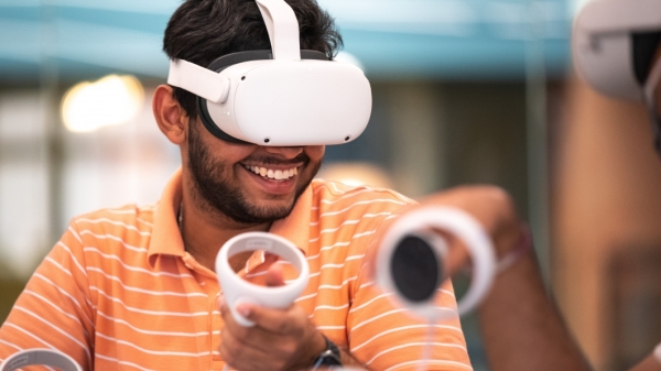 Student in orange polo wearing a virtual reality headset while smiling