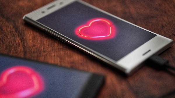 Smartphone sitting on a table. An image of a red heart is displayed on the phone's screen.
