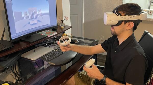 Man wearing a VR headset seated in front of a computer.