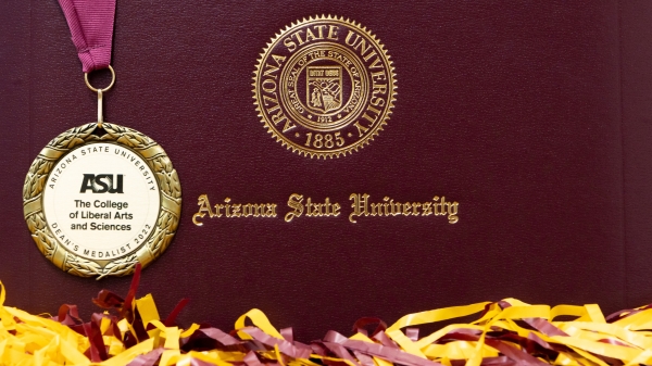 The College 2022 Dean's medal on ASU diploma cover surrounded by sprit gear.