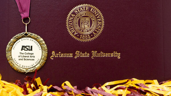 The College 2022 Dean's medal on ASU diploma cover surrounded by sprit gear.