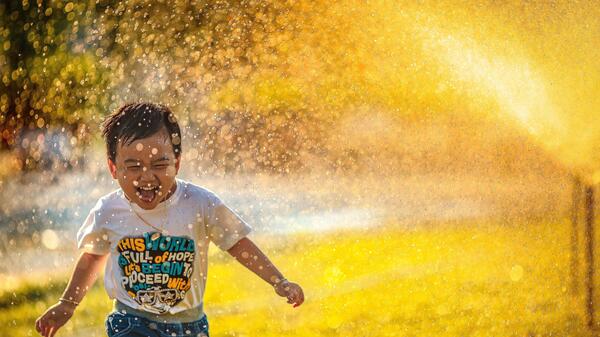 Child running through sprinklers outside.