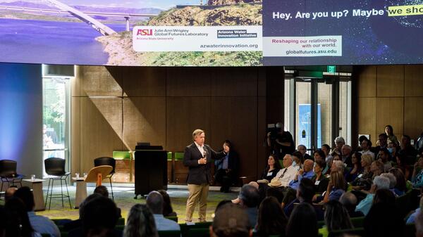 ASU President Michael M. Crow speaks at the Arizona Water Innovation Initiative launch, standing in front of a group of people with a microphone.