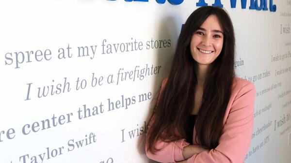 Nicole Waldmann, ASU alum and volunteer coordinator for Make-A-Wish Arizona, stands with arms folded against a wall that reads "Make-A-Wish" 