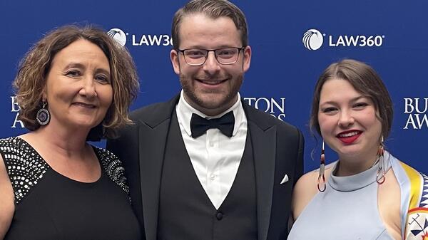 Two women and a man pose for a photo in front of a backdrop. 