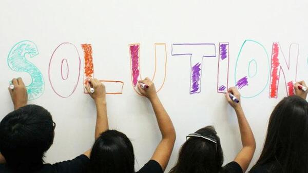 Students write the word "solutions" on a whiteboard in different colored markers.