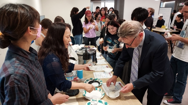 A crowd of people make onigiri along a table