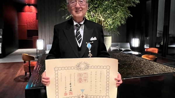 Research Professor Saburo Sugiyama holding up his award and dressed in a black suit and tie.