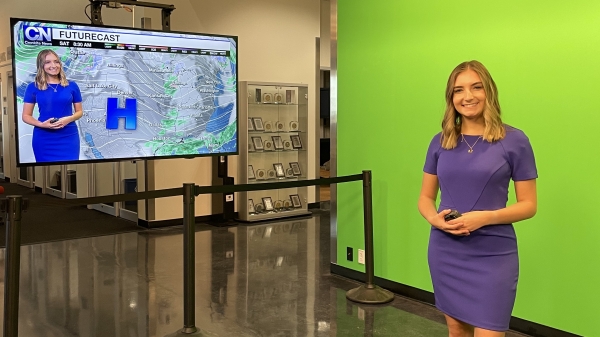 Woman standing in front of a green screen, next to a monitor showing her image and a weather map.
