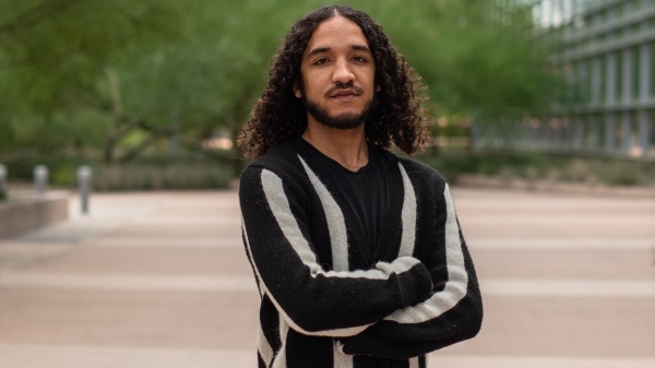 ASU graduate student Dylan Peay stands with arms crossed in the middle of a mall on the Tempe campus