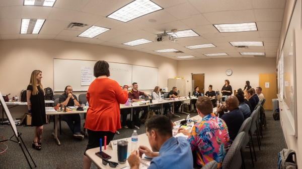 Woman seen from behind speaking to a classroom full of people.