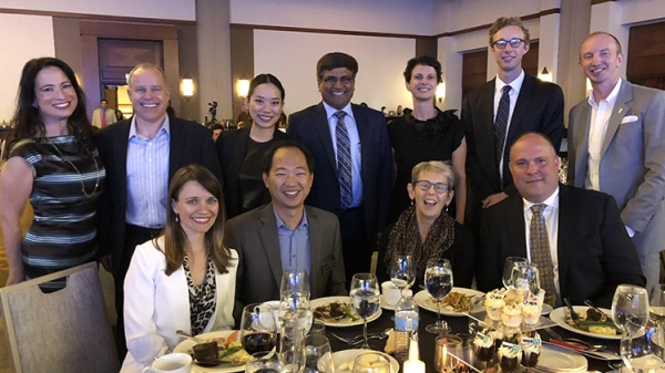 A group of people pose for a photo in a ballroom. Caption reads: Sethuraman Panchanathan poses for a photo with other ASU representatives at the Institute for Automated Mobility event. Photo by Vincent Orleck