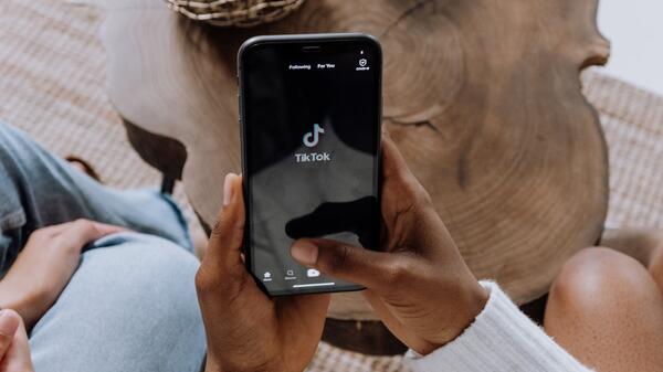 Closeup of a Black woman's hands holding a phone and opening the TikTok platform.