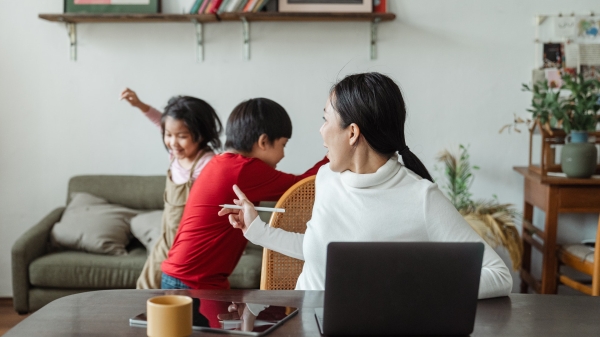 Woman turning around from computer to talk to playing kids at home.