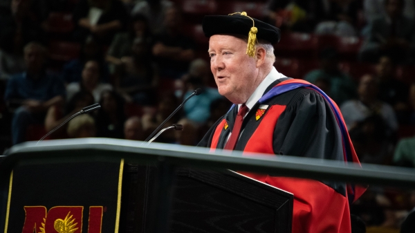 A dean in graduation regalia speaks at a lectern during commencement