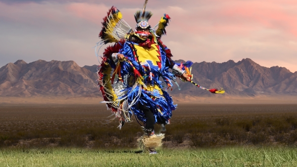 Native American man dressed in traditional, brightly-colored clothing and dancing.