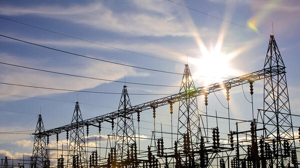 Power lines with the sun shining behind them.