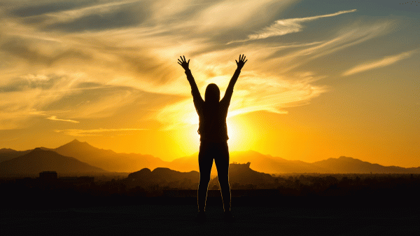 A woman is silhouetted against a desert sunset