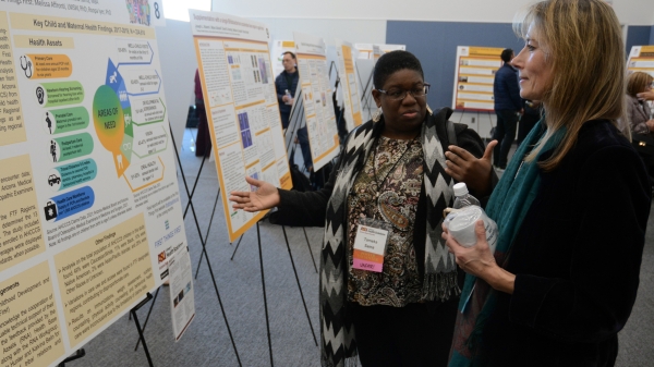 Two attendees at the College of Health Solutions Faculty Research Day talking and looking at presentation posters.