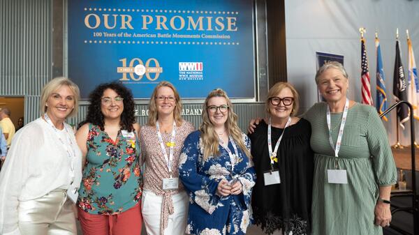 Six women stand shoulder to shoulder smiling into the camera.