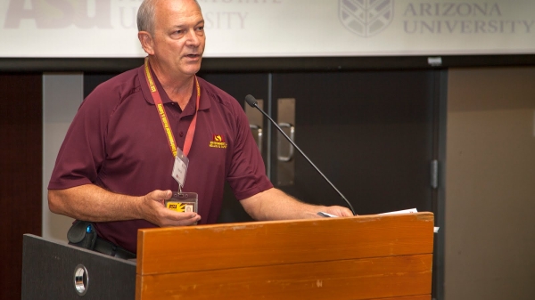 A man addresses a room of attendees from behind a podium. 