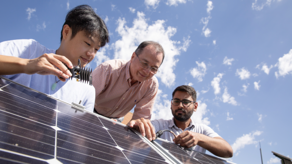 Three people looking at a solar panel.