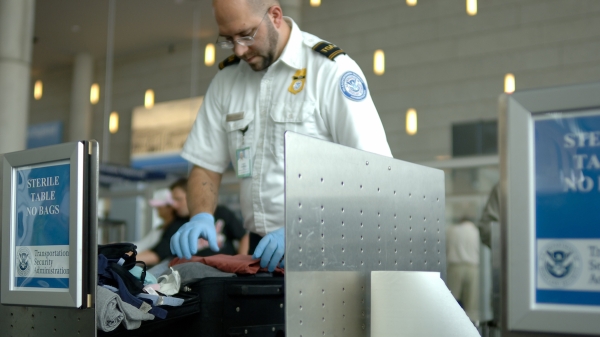 A TSA agent searches luggage at airport security checkpoint.