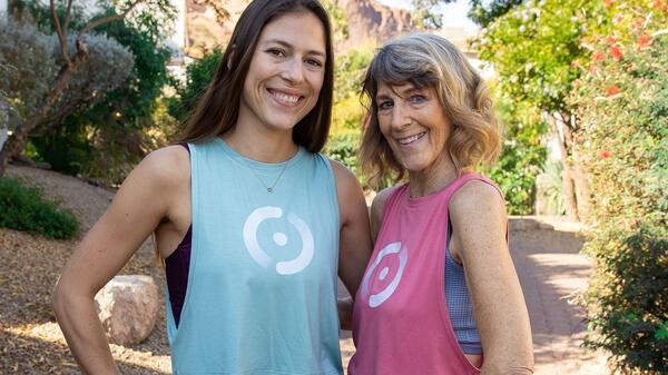 ASU alum Sophie Aigner and her mother, Vickie, pose for a photo on a brick walkway surrounded by greenery and a mountain formation in the background.