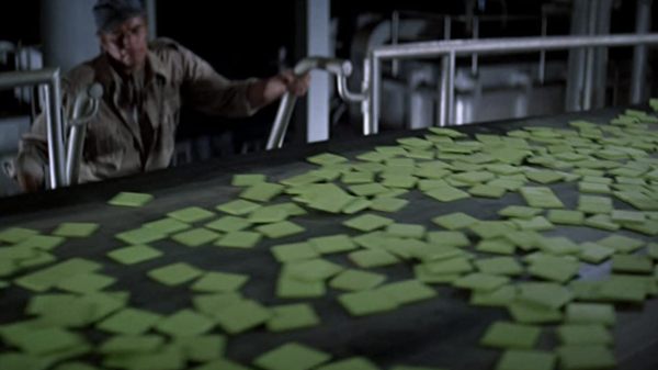 screenshot from movie "Soylent Green" with square green food pieces moving down conveyor belt