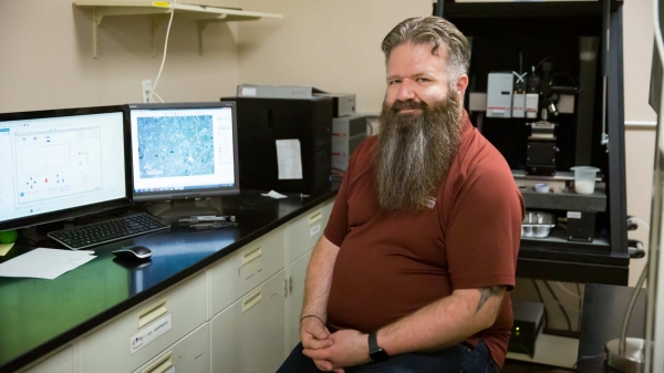 ASU Assistant Professor Christian Hoover sits in his lab in front of a computer and lab equipment.