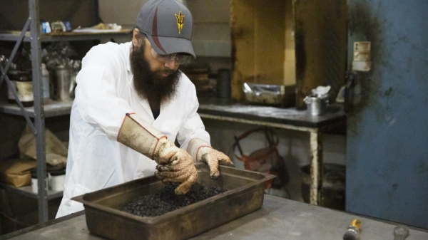 Photograph of graduate student wearing personal protective equipment mixing asphalt with a aggregate base in a giant baking pan